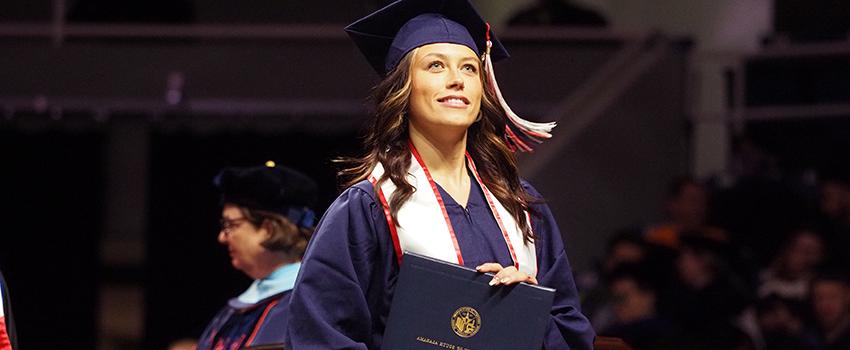 Graduate in cap and gown holding diploma.